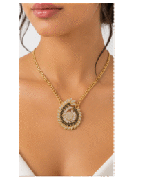 Gold chain necklace with a circular pendant featuring a black geometric center and surrounding diamond accents on a model's décolletage, close-up portrait.